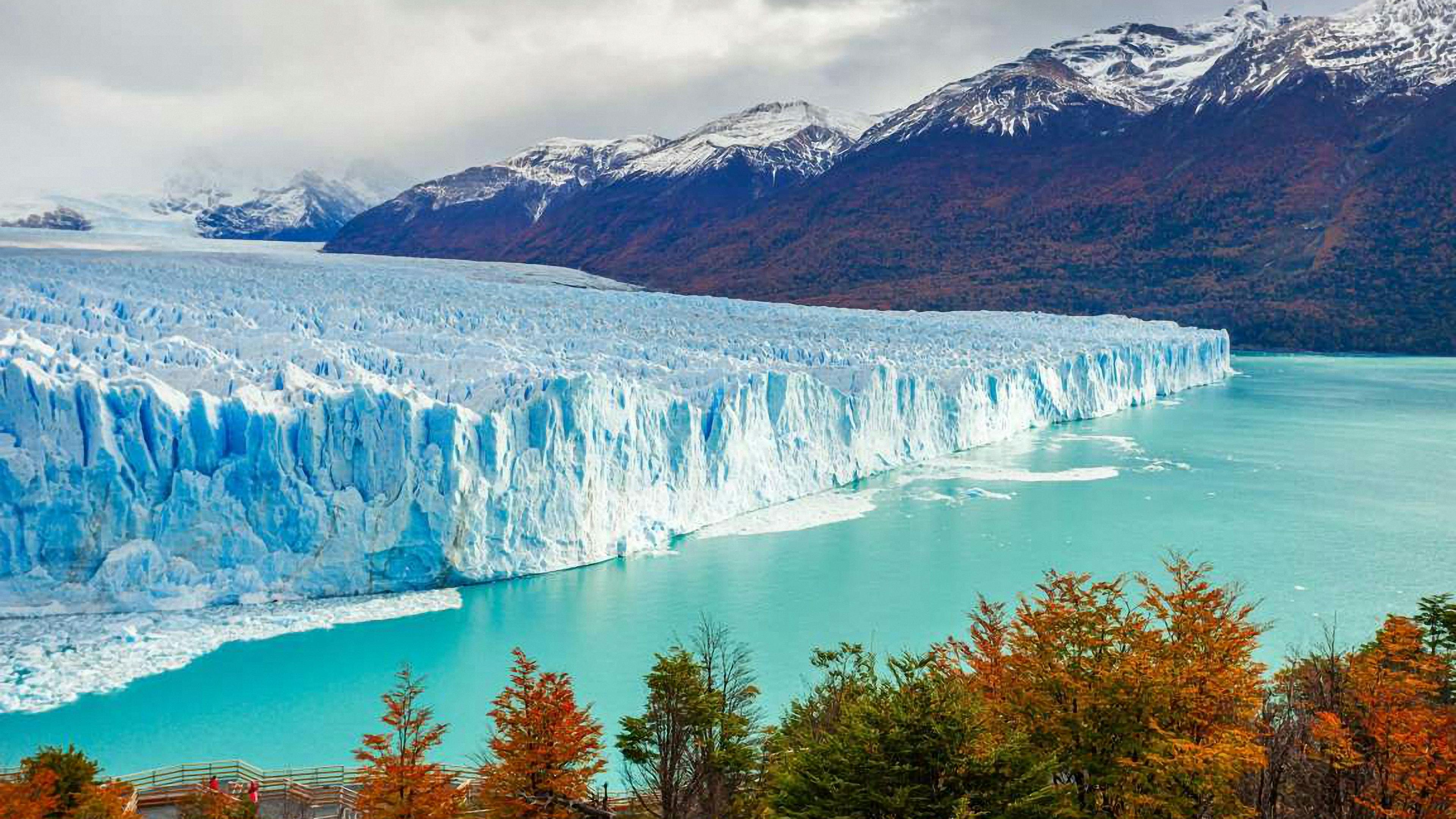 Majestuoso glaciar azul frente a montañas nevadas y lago turquesa